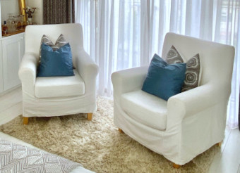 Two comfortable white chairs in front of a bookcase in the treatment room where the initial consultation takes place.